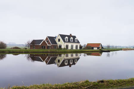 Dutch farmhouse at the side of a lake with reflection in the water near Amsterdam, the Netherlandsの写真素材