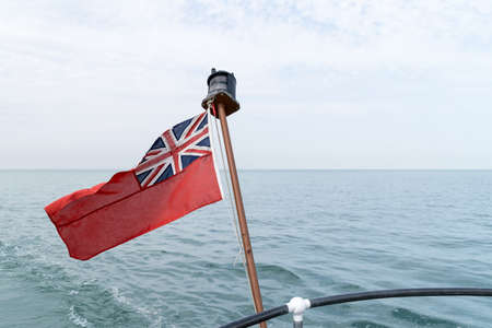 an Uk red ensign the british maritime flag flown from yacht with the sea and sky behind itの写真素材