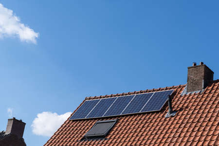 Roof with red roof tiles, chimney and solar panels for making renewable energy and a clear blue sky