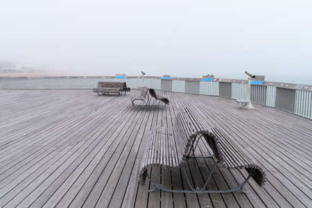 The Pier of Hastings on a misty summer day with benches and telescopes, no people, sea and buildings...