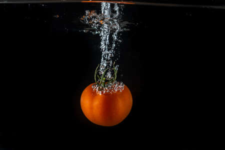 Tomatoes splashing in water on a black backgroundの写真素材