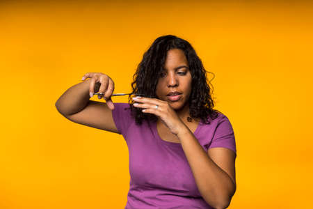 Young attractive mixed race woman cutting her hair in a yellow backgroundの写真素材
