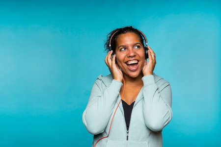 Young attractive mixed race woman enjoying music listening with headphones blue backgroundの写真素材