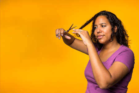 Young attractive mixed race woman cutting her hair in a yellow backgroundの写真素材