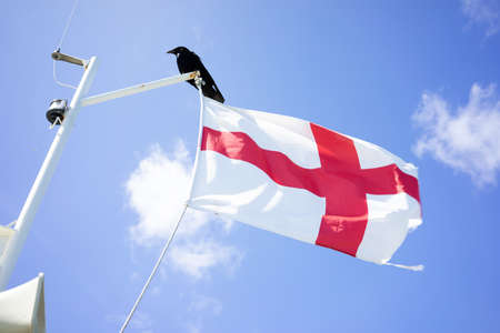 a English flag on a flagpole on a boat against a blue sky with soft clouds in the summerの写真素材