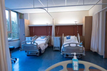 Interior of an empty hospital room with two made beds seen from another bed across the room