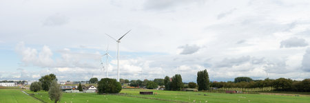 Panorama of Many Windturbines in a Dutch polderlandscape with farms grassland and trees underneath a...