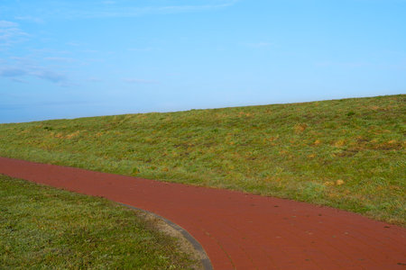 A red cycling path between the green grassland and a blue sky above it