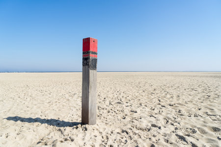 A Close up of a single red beach pole or column on an empty beach at the Dutch North Sea in summer with blue skyの写真素材