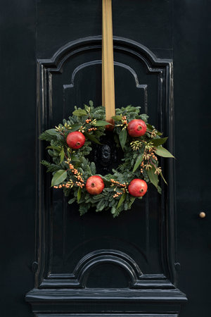 Beautiful door is decorated for Christmas with an evergreen wreath with pomgrenatesの写真素材