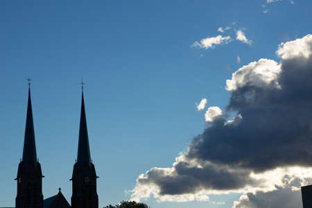 Skyscape with a silhouette of a church cumulus clouds in white and gray and a clear deep blue sky in the summerの写真素材