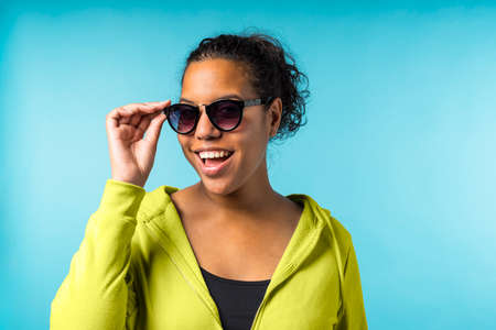 Young attractive mixed race woman with sunglasses in a blue background
