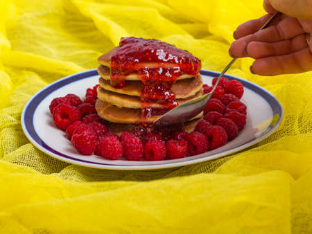 pancakes with ripe raspberries and raspberry jam on a plate spoon and handの写真素材