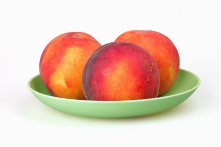 Three ripe peach on a green plate on a white background の写真素材