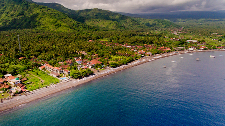 The tropical bay with stony beach, boats and buildings, aerial view. Village of Amed, Bali, Indonesia.の写真素材