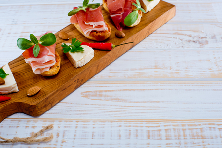 Bruschetta sandwiches with jamon, cheese, almond, chilli papper and green sprouts on a wooden board. White wooden background. の写真素材