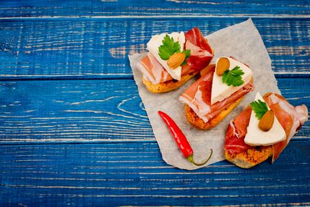Close-up of three sandwiches bruschetta with jamon, cheese, almond, chilli papper and green parsley on blue wooden background.の写真素材