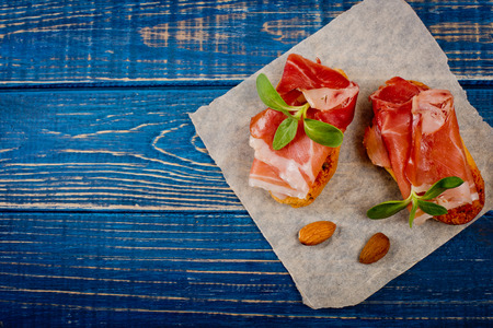 Close-up of two bruschetta sandwiches with jamon, almond and green sprouts on blue wooden background. Top view.の写真素材