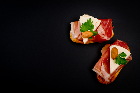 Bruschetta sandwiches with jamon, cheese, almond and parsley. Black background.の写真素材