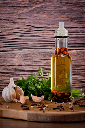 Bottle with olive oil with spices on a wooden background, cloves of garlic and parsley. Backgrounds for the kitchen. Vertical shot.の写真素材