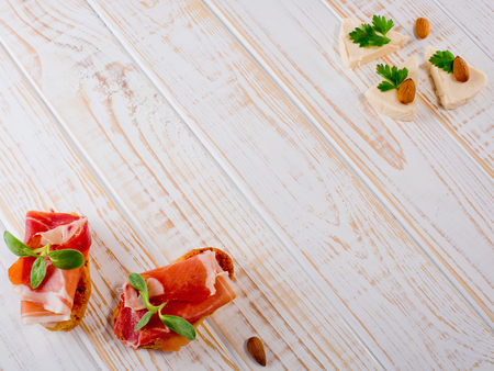 Two bruschetta sandwiches with jamon, green sprouts, almond and cheese on white wooden background.  Frame.の写真素材