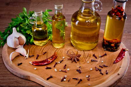 Close-up of bottles with olive oil with spices on a wooden background, cloves of garlic and parsley. Backgrounds for the kitchen.の写真素材