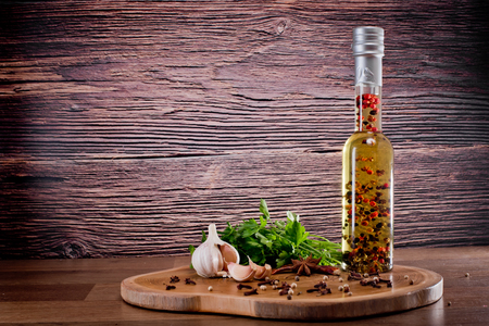 Bottle with olive oil with spices on a wooden background, cloves of garlic and parsley. Backgrounds for the kitchen.の写真素材