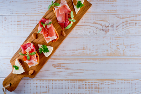 Top view on bruschetta sandwiches with jamon, cheese and green sprouts on a wooden board. White wooden background.の写真素材