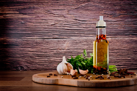 Bottle with olive oil with spices on a wooden background, cloves of garlic and parsley. Backgrounds for the kitchen.の写真素材