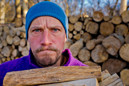 Close-up portrait of a serious lumberjack man holding firewood.の写真素材