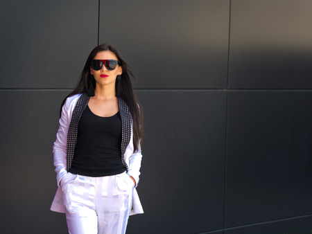Portrait of a beautiful brunette with glasses that stands near a black wall.