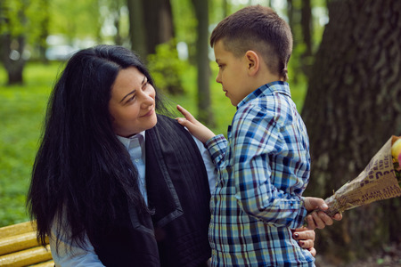 The son gives his mother a fresh bouquet of tulips flowers on a bench in the park. Family photo session.の写真素材