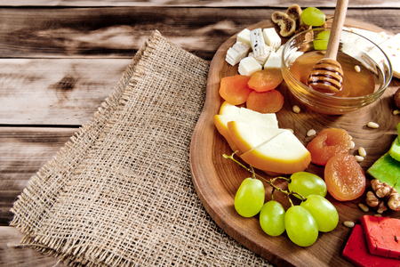 Cheese plate - various types of cheese, honey, grapes, dried apricots, nuts and figs on a wooden board on dark wooden background.の写真素材