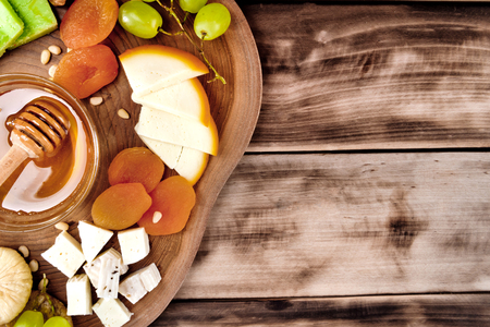 Cheese plate - various types of cheese, honey, grapes, dried apricots, nuts and figs on a wooden board on dark wooden background.の写真素材