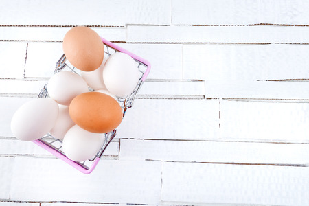 Ð¡hicken eggs in metal shopping basket on white wooden background.の写真素材