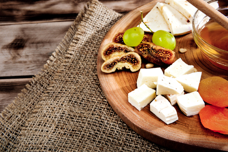 Cheese plate - various types of cheese, honey, grapes, dried apricots, nuts and figs on a wooden board on dark wooden background.の写真素材