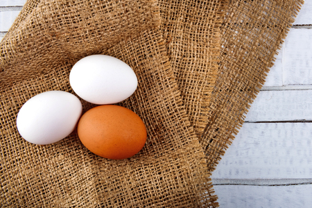 Chicken eggs on sackcloth tablecloth on white wooden background.の写真素材