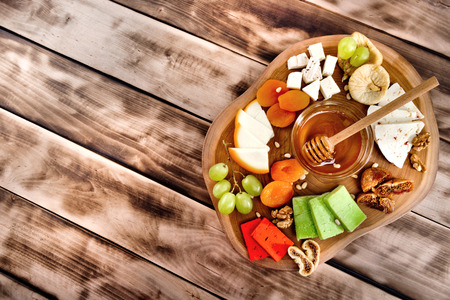 Cheese plate - various types of cheese, honey, grapes, dried apricots, nuts and figs on a wooden board on dark wooden background.の写真素材