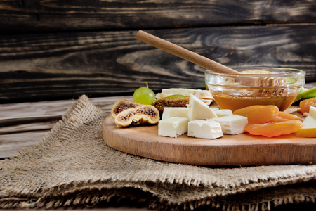 Cheese plate - various types of cheese, honey, grapes, dried apricots, nuts and figs on a wooden board on dark wooden background.の写真素材