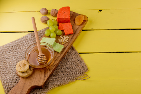 Ð¡heese plate - various types of cheese, honey, grapes, dried apricots, nuts and figs on a wooden board on yellow wooden background.の写真素材