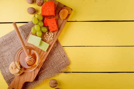 Ð¡heese plate - various types of cheese, honey, grapes, dried apricots, nuts and figs on a wooden board on yellow wooden background.の写真素材