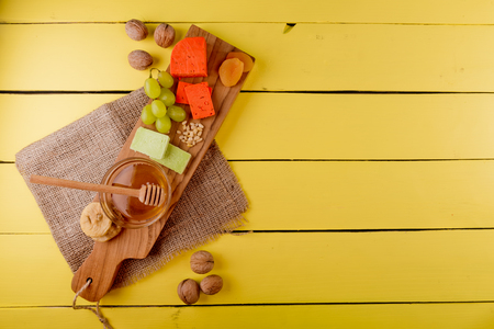 Ð¡heese plate - various types of cheese, honey, grapes, dried apricots, nuts and figs on a wooden board on yellow wooden background.の写真素材