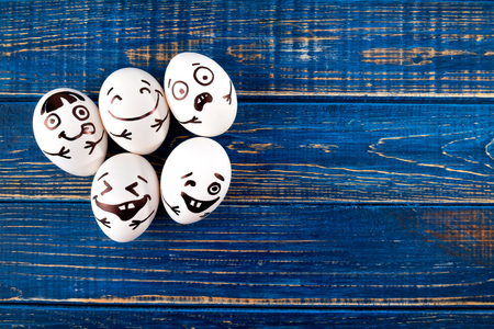 Funny easter eggs with different funny faces on blue wooden background. Top view.の写真素材