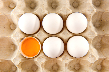Whole white chicken eggs and one broken egg in tray.の写真素材