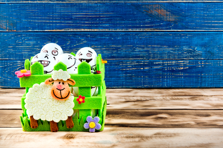 Funny easter eggs with different funny faces in the basket on blue and wooden background.の写真素材