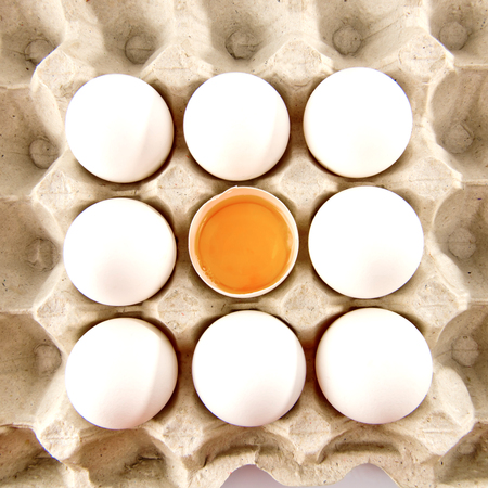 Whole white chicken eggs and one broken egg in tray.の写真素材