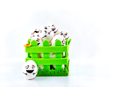 Funny easter eggs with different funny faces in the green basket on white background.の写真素材