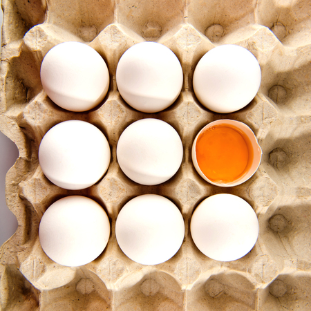 Whole white chicken eggs and one broken egg in tray.の写真素材