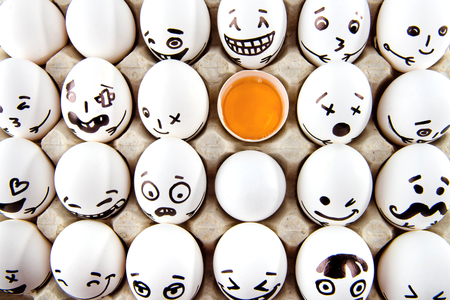 Eggs with drawn cartoon faces and one broken egg in tray. の写真素材