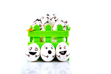 Funny easter eggs with different funny faces in the green basket on white background.の写真素材